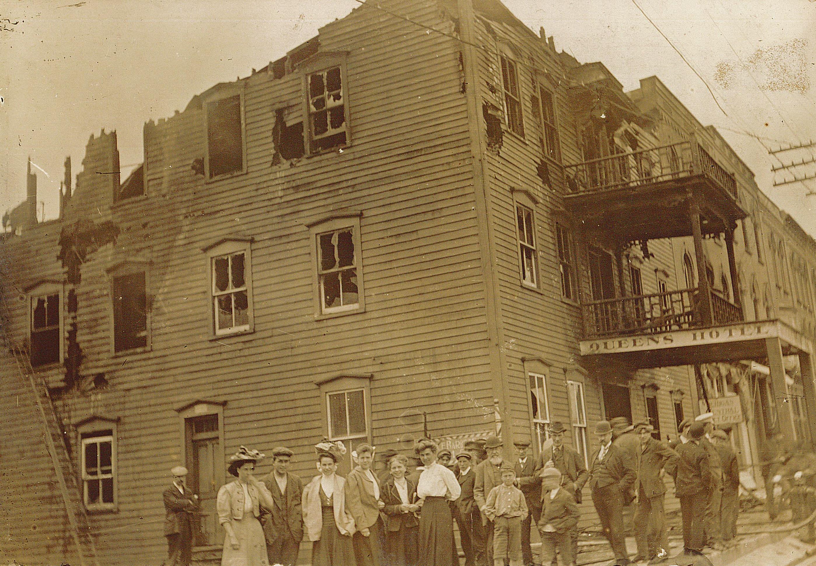 Photo of the Queen's Hotel damaged by fire, a crowd is posed in front of the building.