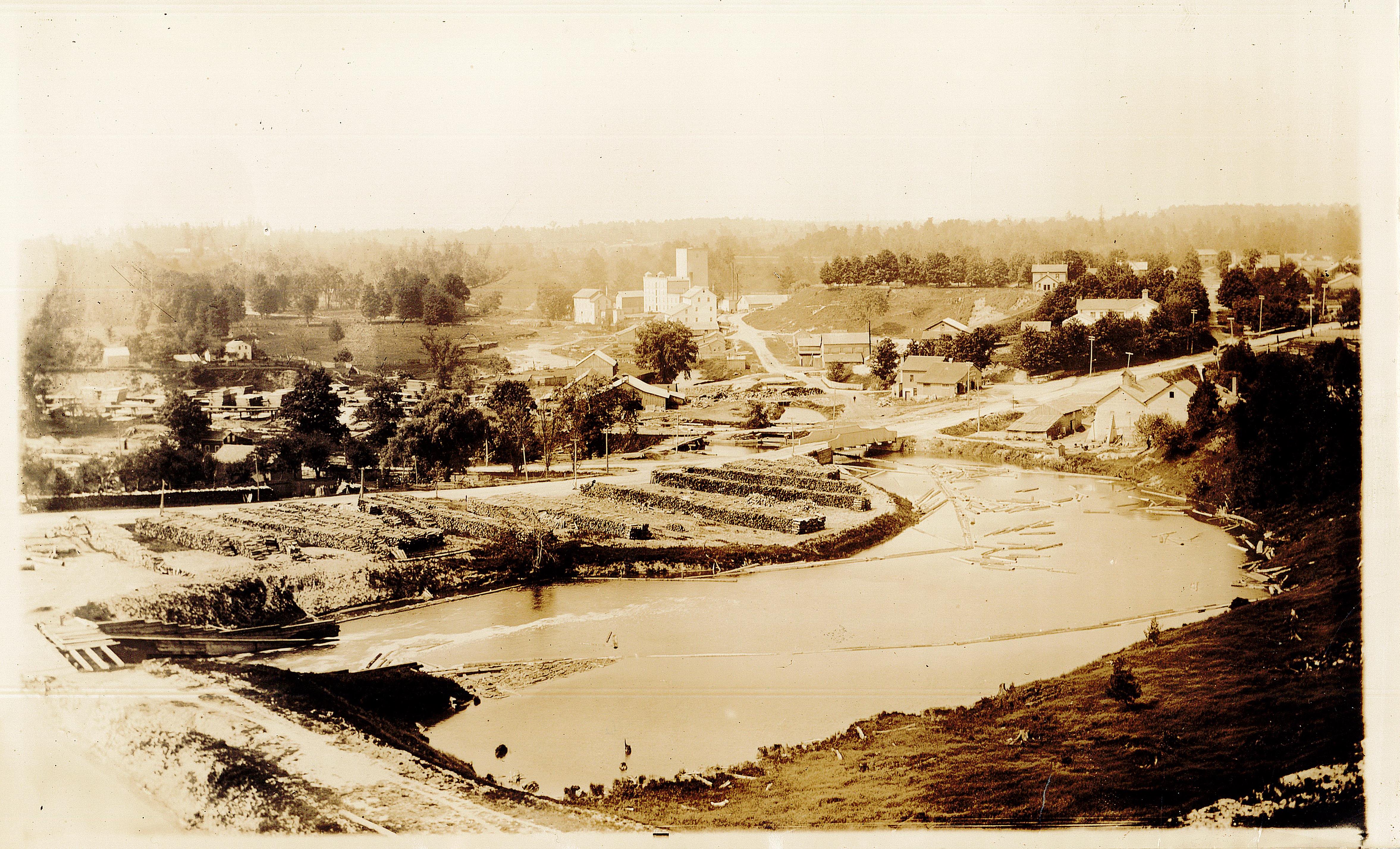 Aerial view of the Tillson mills. A large, light coloured mill is in the distance, with a creek in the foreground. Smaller buildings and trees dot the landscape.